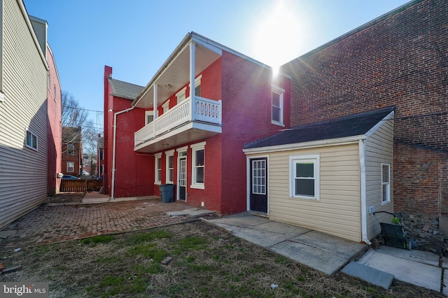 rear view of property with brick siding, a balcony, and a patio