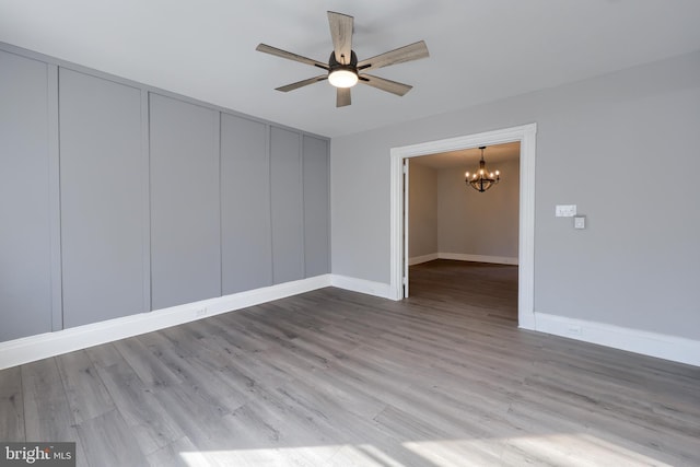 unfurnished room featuring ceiling fan with notable chandelier, baseboards, and wood finished floors