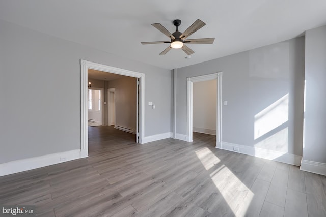 spare room featuring wood finished floors, a ceiling fan, baseboards, and a baseboard radiator