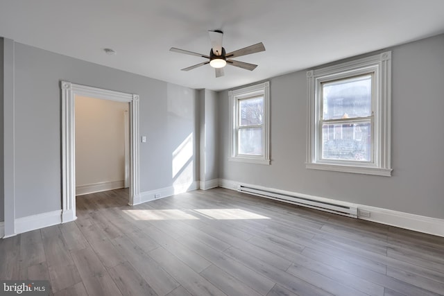 empty room featuring baseboard heating, ceiling fan, baseboards, and wood finished floors