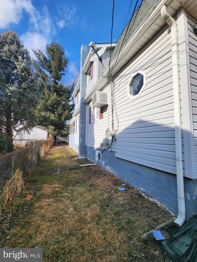 view of property exterior featuring a lawn, a chimney, a wall unit AC, and fence