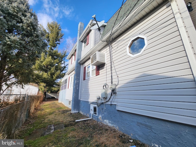 view of side of property featuring a wall mounted air conditioner, a chimney, and fence