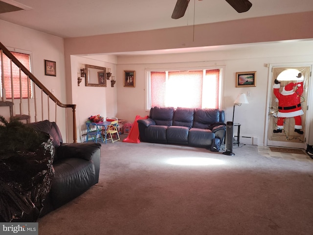 living area featuring stairway, carpet floors, baseboard heating, and a ceiling fan