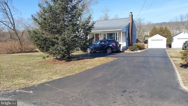 view of front of property with an outbuilding, a chimney, a detached garage, and a front yard