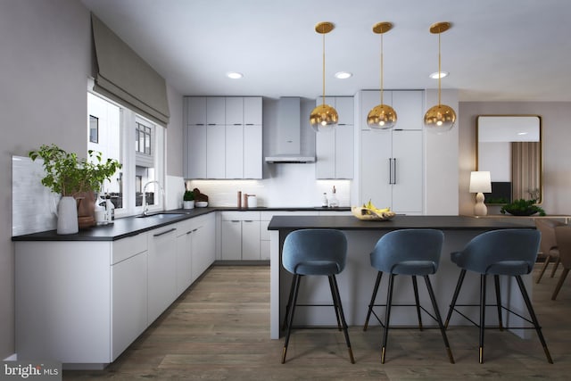 kitchen featuring dark countertops, a breakfast bar area, wall chimney range hood, and a sink