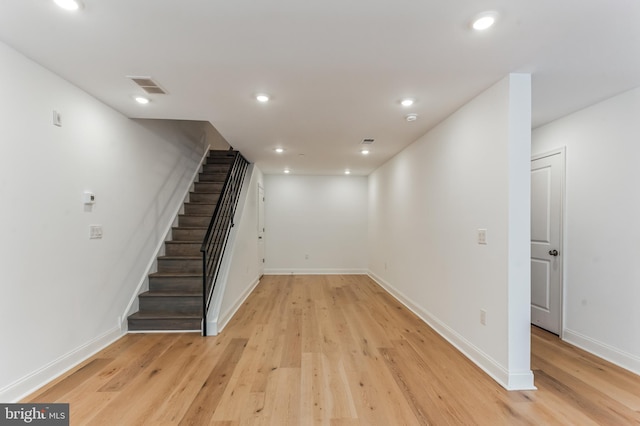 finished basement featuring recessed lighting, visible vents, light wood-style flooring, and stairway
