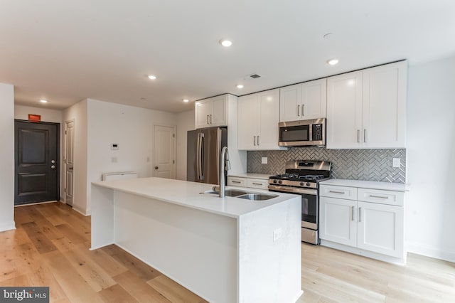 kitchen with a center island with sink, stainless steel appliances, light wood-style floors, white cabinetry, and a sink