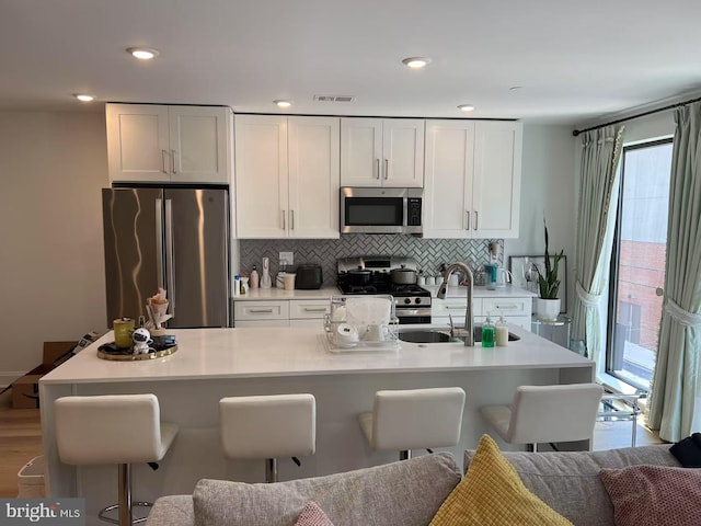 kitchen with a breakfast bar area, stainless steel appliances, decorative backsplash, light countertops, and white cabinets