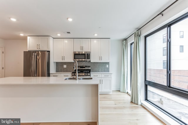 kitchen with a sink, decorative backsplash, light countertops, stainless steel appliances, and white cabinetry