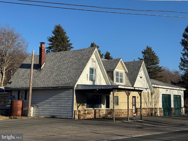 view of front facade featuring stone siding, roof with shingles, and a chimney