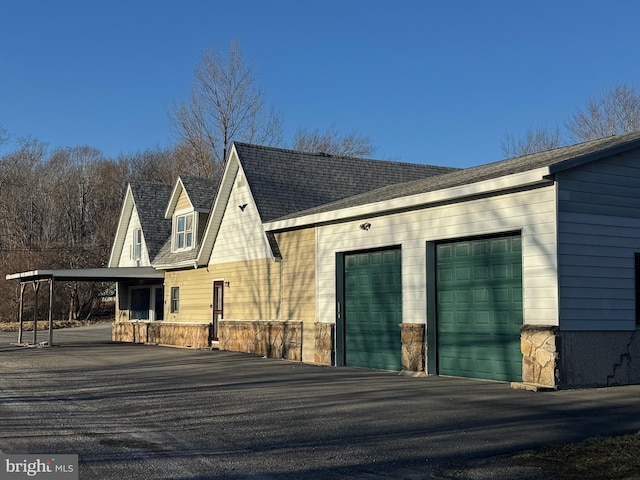 exterior space with a garage, stone siding, and a shingled roof