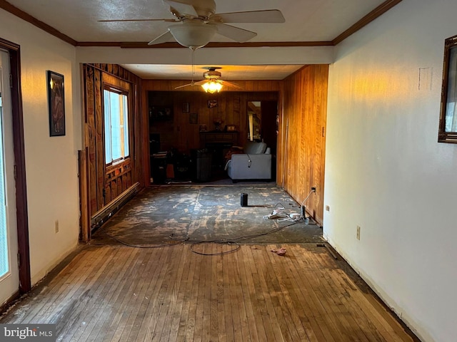 unfurnished living room featuring wood-type flooring, baseboard heating, ornamental molding, and wood walls