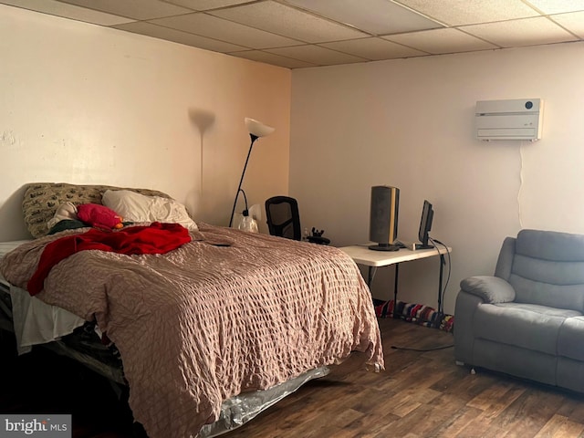 bedroom featuring a drop ceiling, an AC wall unit, and wood finished floors