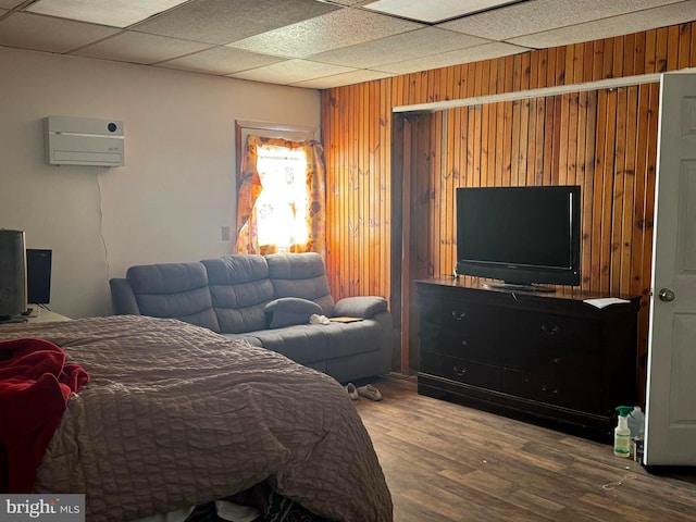 bedroom with a drop ceiling, wood walls, an AC wall unit, and wood finished floors