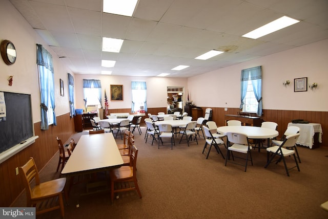 carpeted dining room with a paneled ceiling, wood walls, and wainscoting