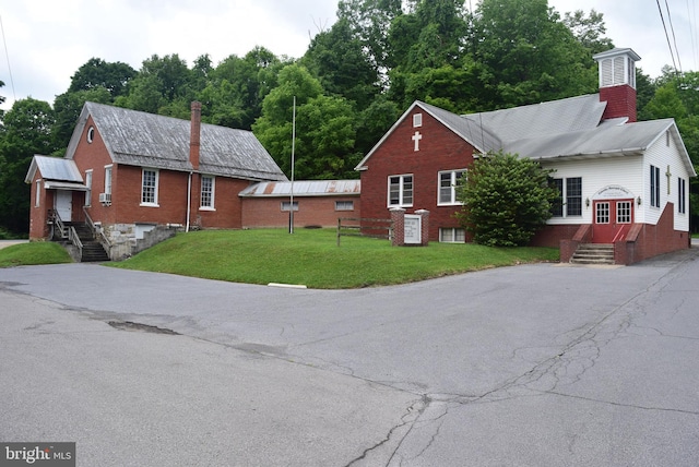 view of property exterior featuring brick siding, entry steps, a chimney, and a yard