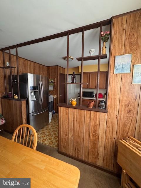 kitchen featuring brown cabinetry, stainless steel fridge, a peninsula, and dark countertops