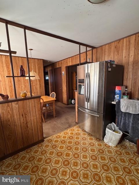 kitchen with brown cabinetry, wooden walls, and stainless steel fridge