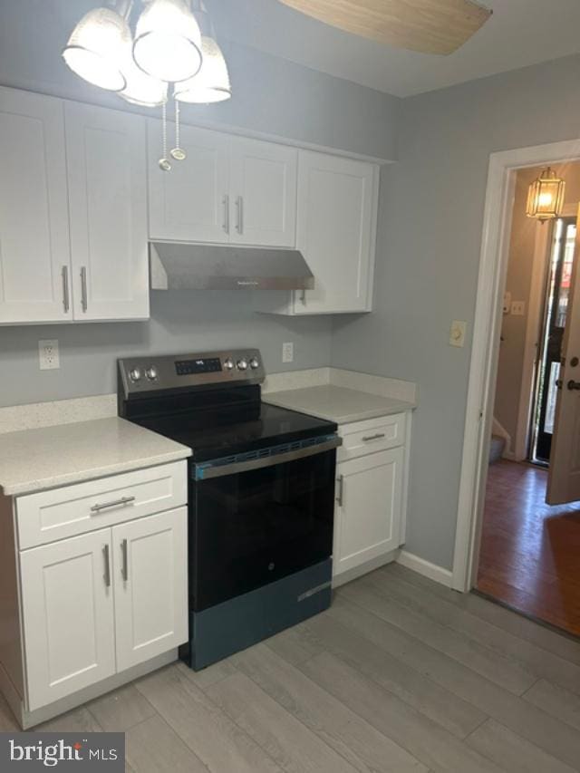 kitchen with under cabinet range hood, stainless steel electric stove, light countertops, light wood-style flooring, and white cabinets