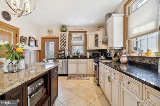 kitchen featuring light tile patterned floors, decorative backsplash, cream cabinetry, stainless steel appliances, and a sink