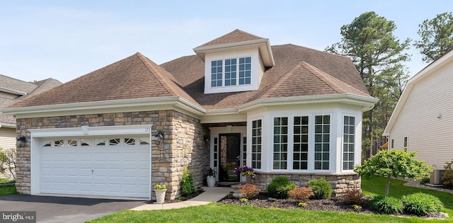 view of front facade with driveway, a garage, cooling unit, a shingled roof, and stone siding
