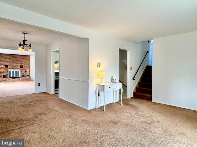 unfurnished living room featuring a notable chandelier, a brick fireplace, stairs, and carpet floors