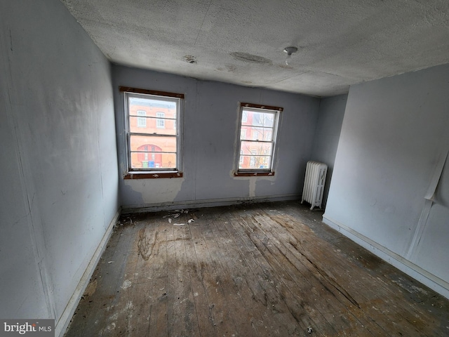 empty room featuring hardwood / wood-style flooring, radiator heating unit, and a textured ceiling