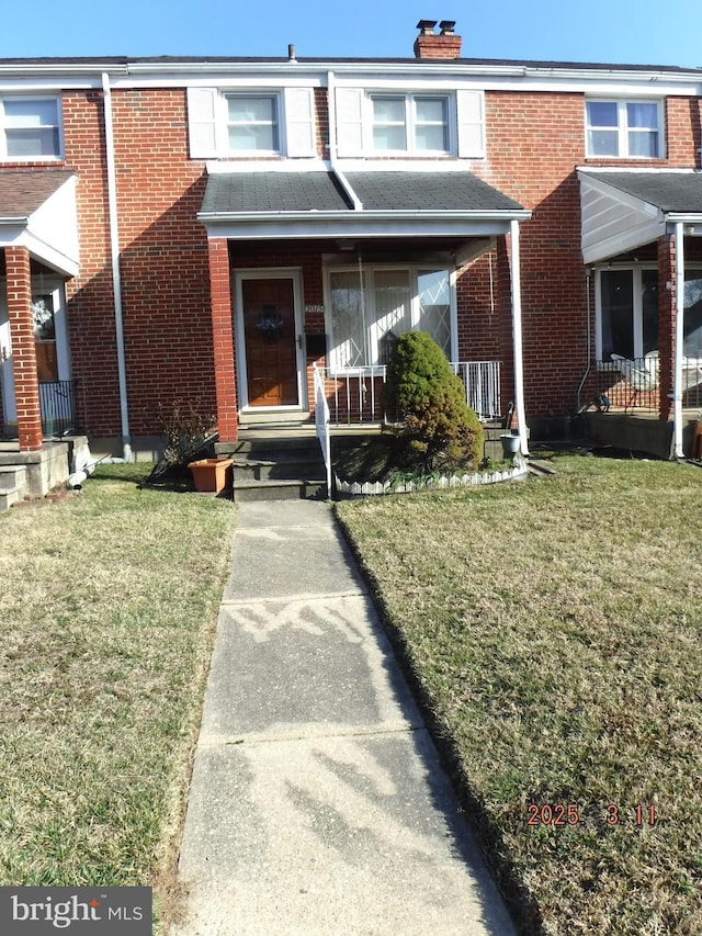 townhome / multi-family property featuring a porch, brick siding, a chimney, and a front lawn