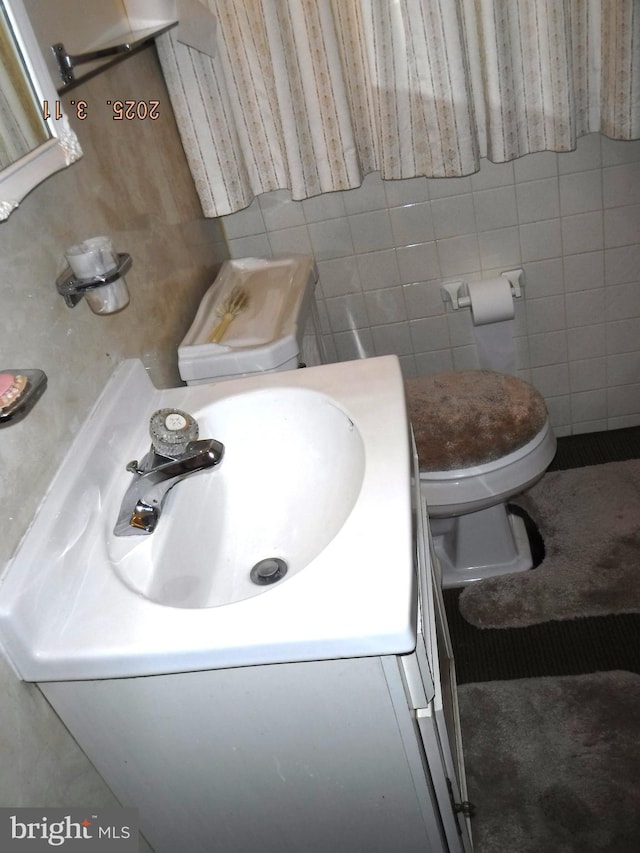 bathroom featuring vanity, tile walls, and toilet