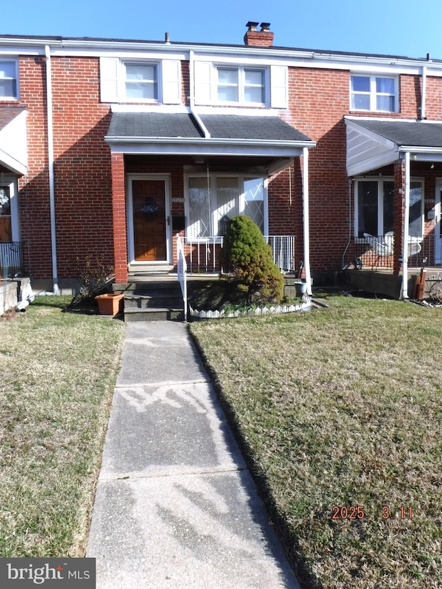 multi unit property with brick siding, covered porch, a chimney, and a front lawn