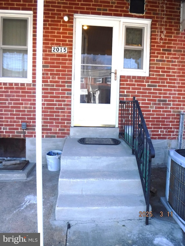 doorway to property with brick siding and central AC