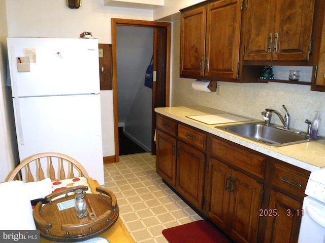 kitchen featuring a sink, freestanding refrigerator, light countertops, decorative backsplash, and light floors