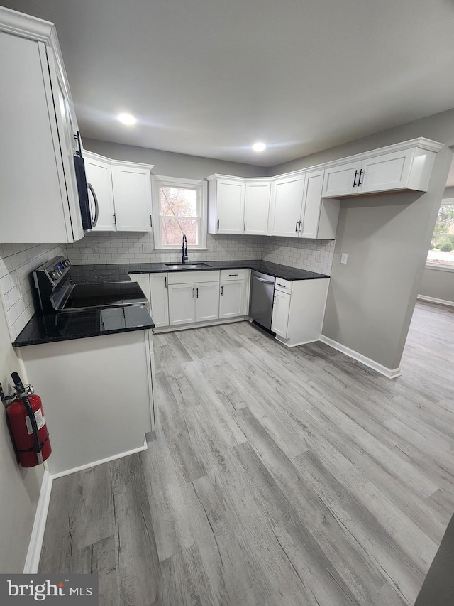 kitchen with a sink, dark countertops, backsplash, stainless steel appliances, and light wood-style floors