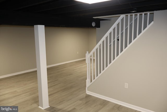 finished below grade area featuring stairs, wood finished floors, and baseboards