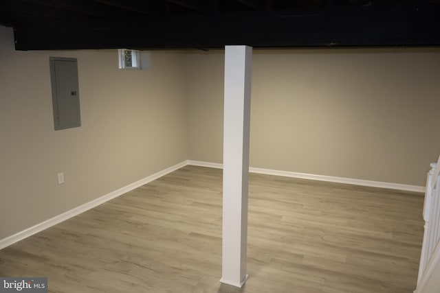 finished below grade area featuring electric panel, light wood finished floors, and baseboards