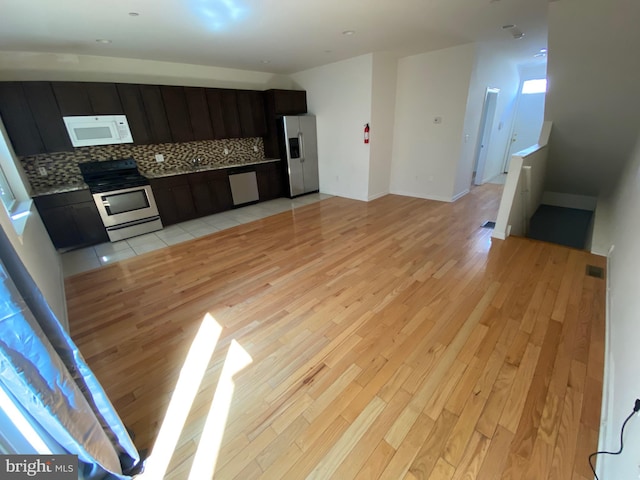 kitchen with light wood finished floors, stainless steel appliances, open floor plan, tasteful backsplash, and dark cabinets