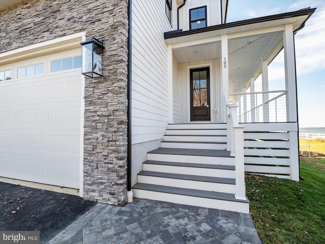 doorway to property featuring board and batten siding, a porch, a garage, and stone siding