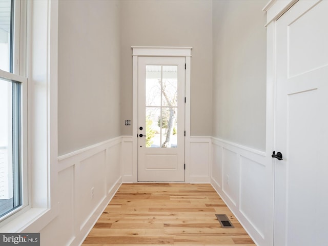 doorway with a wainscoted wall, a decorative wall, visible vents, and light wood finished floors