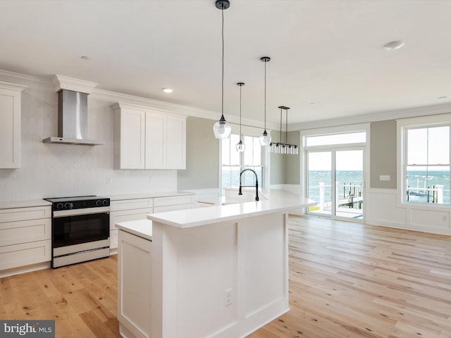 kitchen with an island with sink, light countertops, range with electric stovetop, wall chimney exhaust hood, and light wood-type flooring