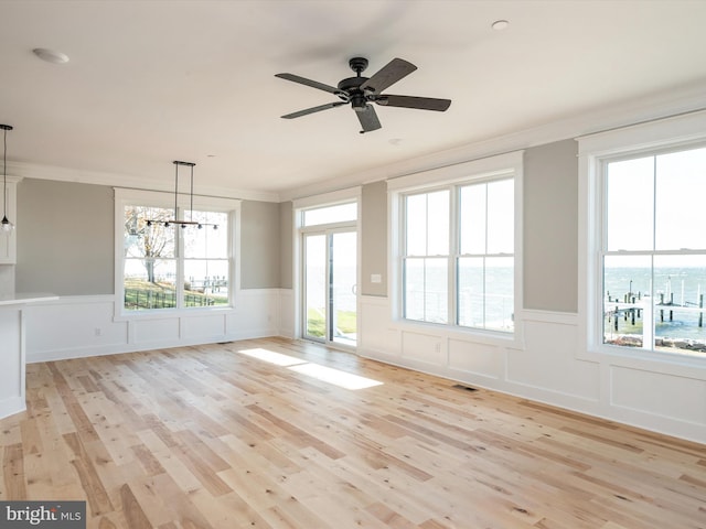 empty room featuring light wood-style floors, wainscoting, crown molding, and ceiling fan with notable chandelier