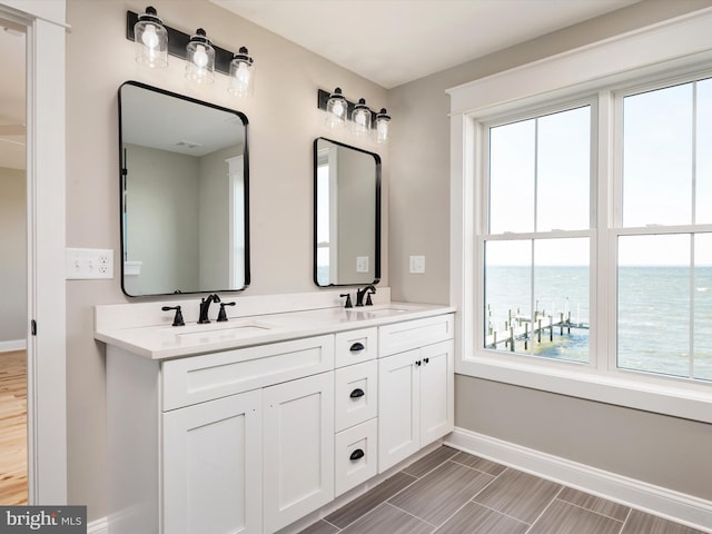 full bathroom with double vanity, a healthy amount of sunlight, baseboards, and a sink