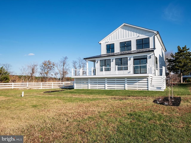 rear view of house with board and batten siding, a yard, and fence