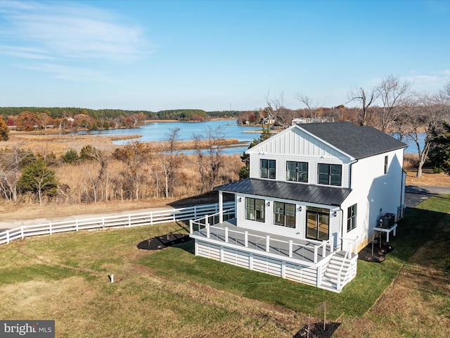 exterior space featuring fence, board and batten siding, a water view, and a lawn