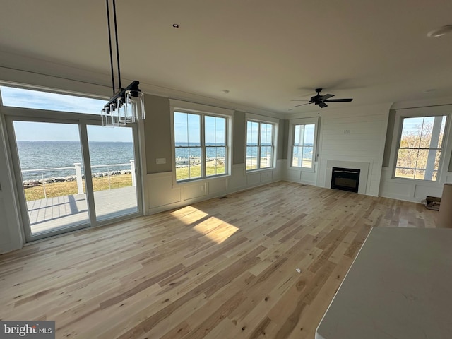 unfurnished living room with light wood-type flooring, a water view, a ceiling fan, a large fireplace, and a decorative wall