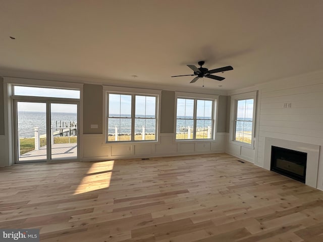 unfurnished living room featuring a decorative wall, a water view, a fireplace, and light wood finished floors