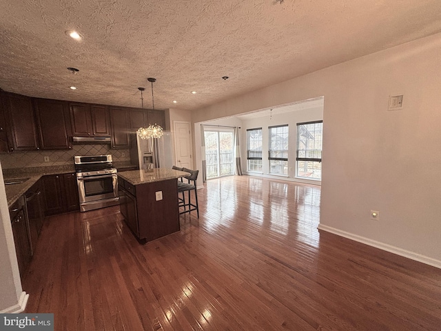 kitchen featuring baseboards, a breakfast bar, dark wood-style flooring, stainless steel gas range oven, and tasteful backsplash