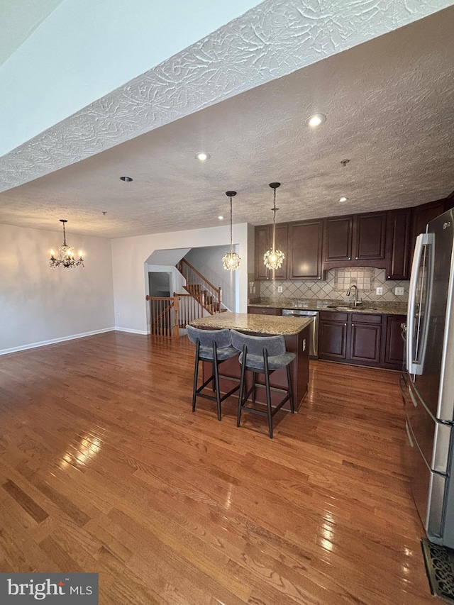 kitchen featuring a sink, decorative backsplash, dark wood-type flooring, stainless steel appliances, and a notable chandelier