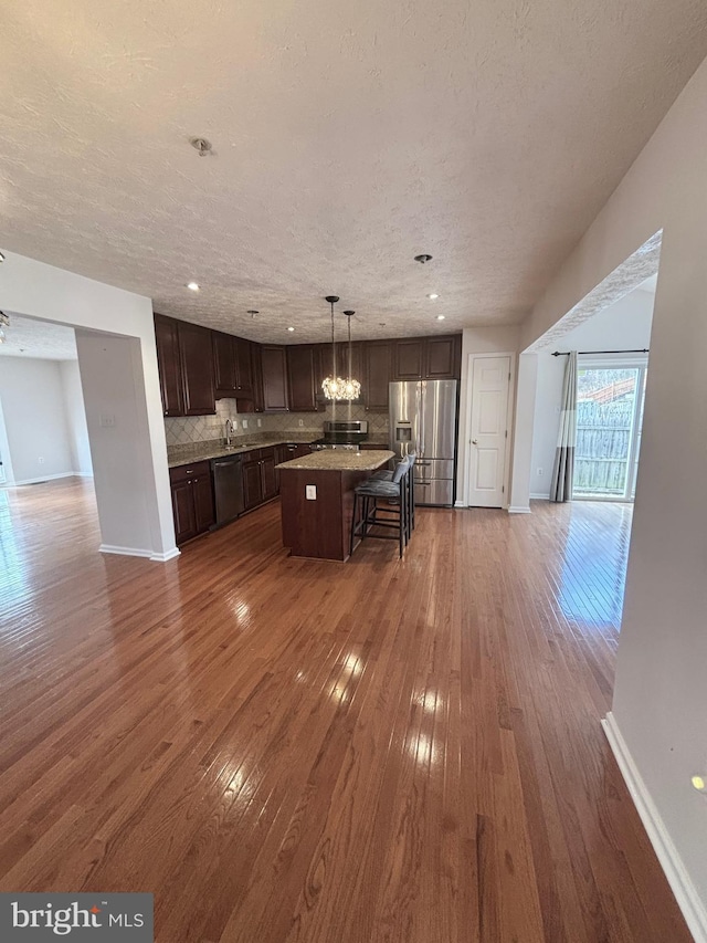 kitchen with backsplash, open floor plan, stainless steel fridge, dark brown cabinets, and dishwasher