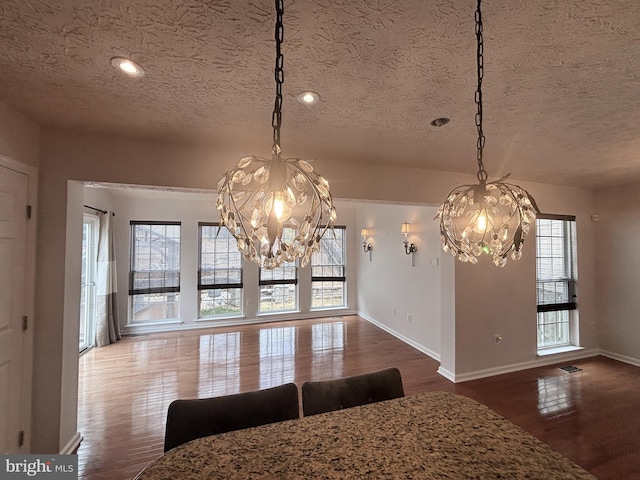 unfurnished dining area featuring an inviting chandelier, wood finished floors, baseboards, and a textured ceiling