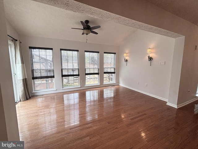 unfurnished living room featuring baseboards, a textured ceiling, hardwood / wood-style floors, and vaulted ceiling